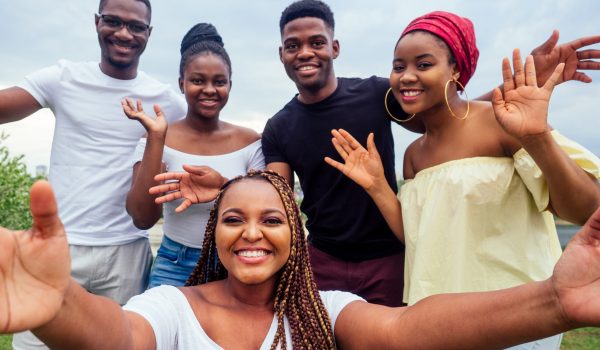 group of five friends female and male taking selfie on camera smartphone and having fun outdoors lifestyle near lake